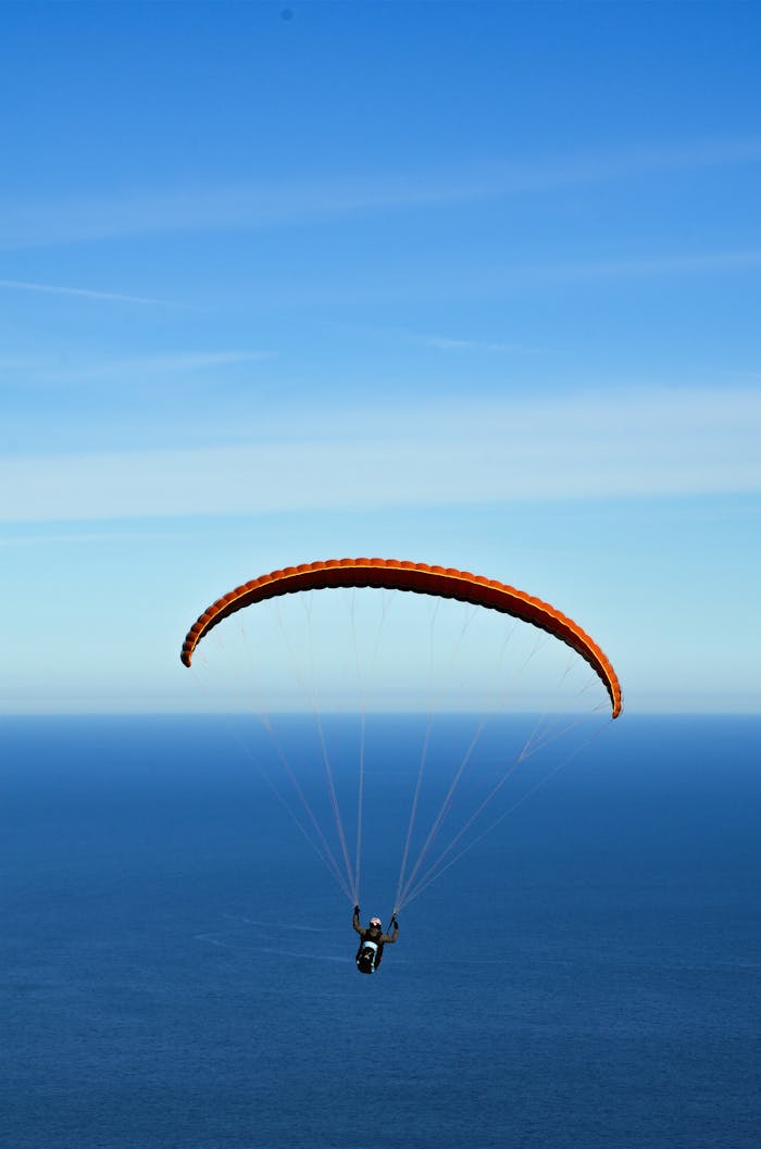 Mastering the First Impression: Your intriguing post title goes here A person paragliding with an orange chute over a vast ocean under clear blue skies.